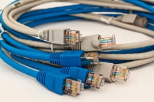 A close-up view of several blue and gray Ethernet cables with clear plastic connectors, coiled together on a white surface.