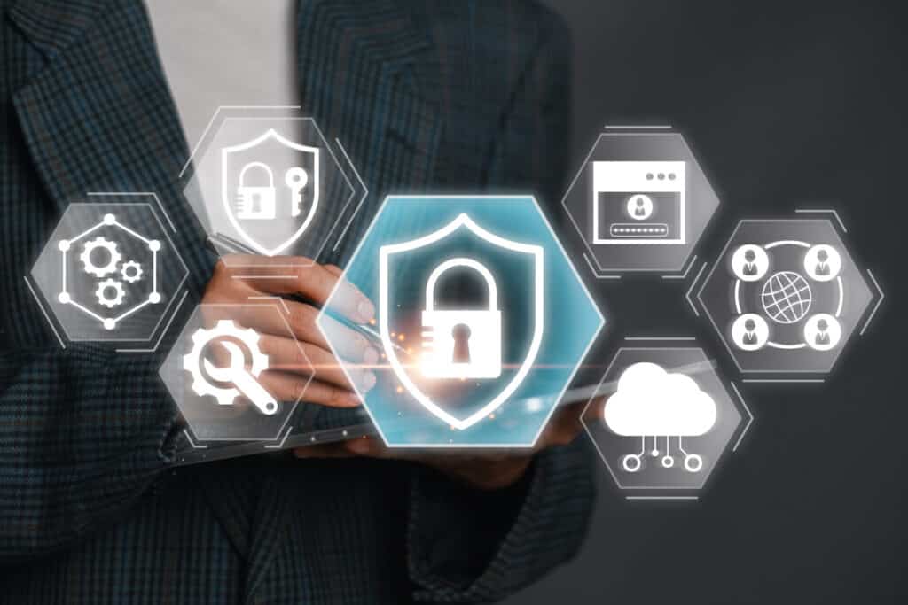 A person in a suit holds a tablet with translucent digital icons—padlock, cloud, gear, and network—representing cybersecurity.
