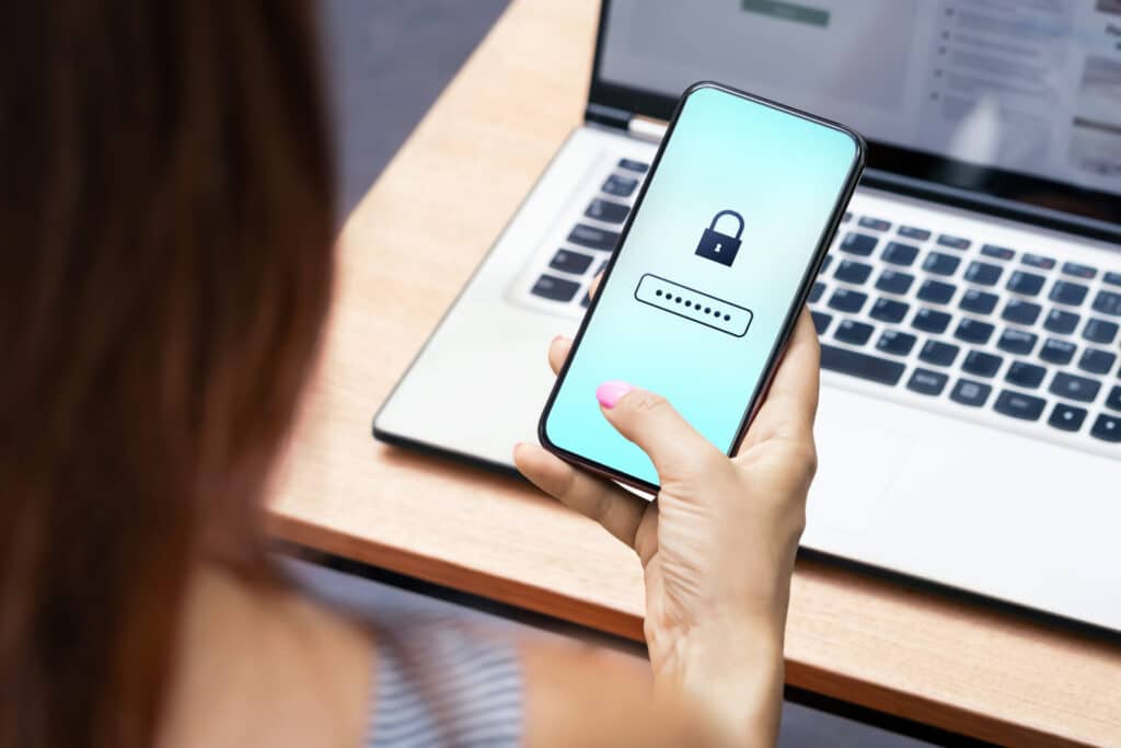 Closeup of a woman in front of her laptop with her phone in her hand. She is typing in a password.
