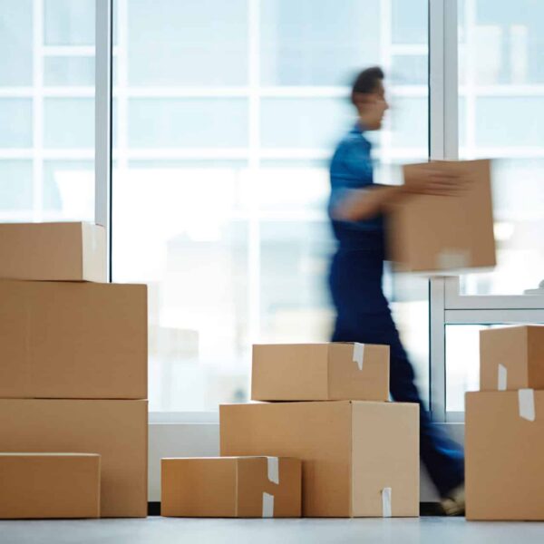 Image of a commercial space filled with lots of stacked moving boxes. A mover is carrying a box across the otherwise empty room