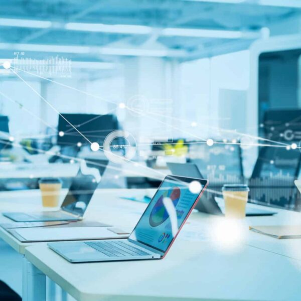 Modern open-plan office with laptops on desks, coffee cups, and digital data graphics overlaying the scene to show connectivity.