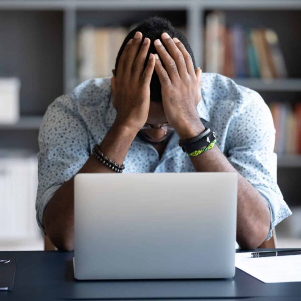African American man sitting at his desk in front of a lap top with his head in his hands. Indicates frustration with slow network and cabling problems.