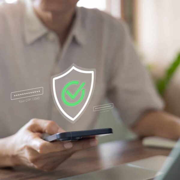 Closeup of a man using his phone and computer to complete a multi-factor authentication process to login to an account online.