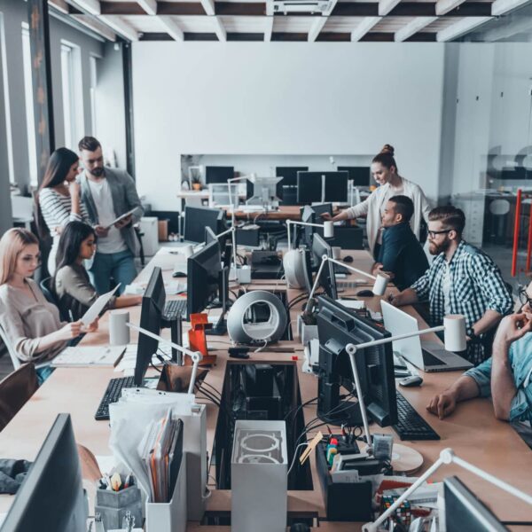 A group of colleagues working at a large shared desk in a modern, open-plan office. Indicates a growing business in need of cybersecurity best practices.
